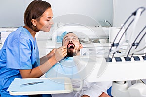 Stomatologist girl in uniform is taking visional inspection of a man