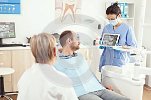 Stomatologist nurse in gloves holding tablet showing jaw x-ray to sick patient