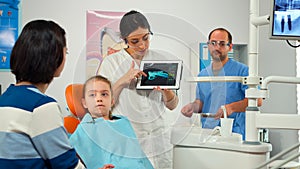 Stomatologist pointing on digital screen explaining x-ray to mother