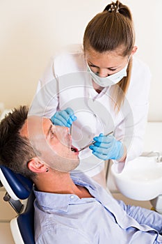 Stomatologist in uniform is taking visional inspection of an adult patiant on the chair