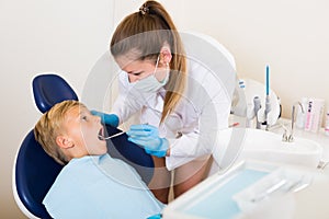 Stomatologist in uniform is taking visional inspection of a teenager on the chair