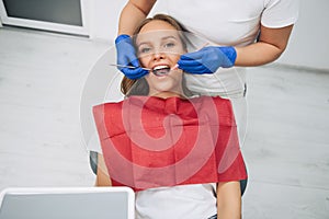 Stomatology and health care concept - happy female dentist with mirror checking patient girl teeth up at dental clinic office.