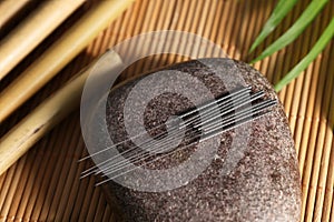 Stone with acupuncture needles on bamboo mat, above view