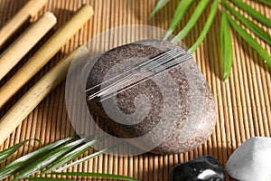 Stone with acupuncture needles on bamboo mat, above view