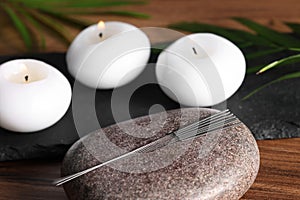 Stone with acupuncture needles and burning candles on wooden table