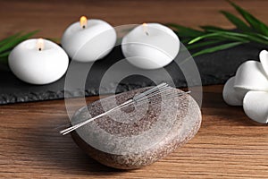 Stone with acupuncture needles and burning candles on wooden table
