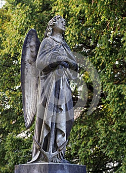 Stone angel, draped, winged, barefoot, holding anchor.