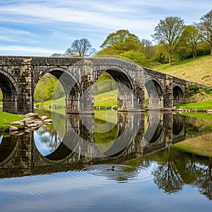 Stone arch bridge spans a tranquil river, with clear reflections in the water. The