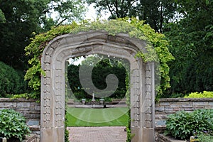 A stone arch entry, covered in a vine, leading to the sunken garden, flanked by flagstone raised flower beds in Janesville, WI