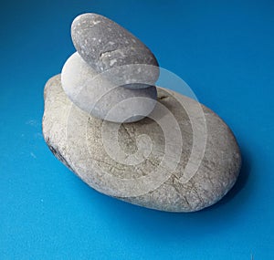 Stone balance with three different sized stones over blue background. Pebbles stack.