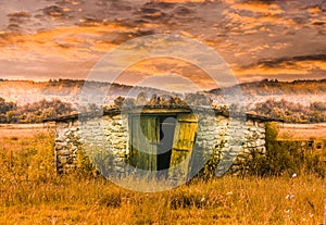 Stone barn building in the grass field at sunset. Abandoned old shed in fairy tale scene. Styled stock photo with the countryside