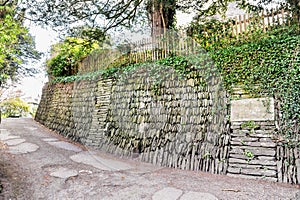 Stone based slope with wooden fance on it and the old road