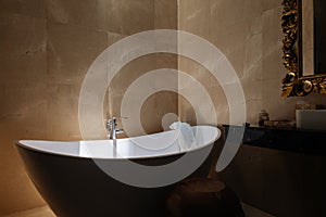 Stone bath tub in luxury interior hotel with sun light from top. Organic spa relaxation in Bali bathroom.