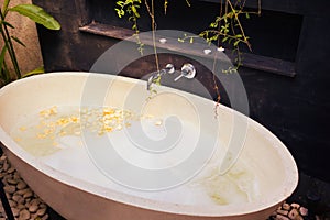 Stone bath tub with water, soap bubbles and petals