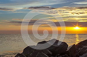 stone beach on the background of the sea, sunset in the clouds.