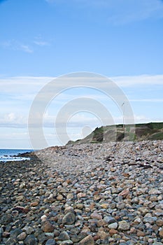 Stone beach by the sea. Flagpole with Danish flag on a hill. Danish coast