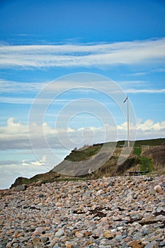 Stone beach by the sea. Flagpole with Danish flag on a hill. Danish coast