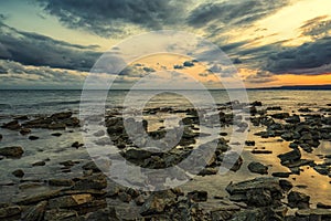 Stone beach at sunset. Twilight sea and sky. Dramatic sky and clouds.