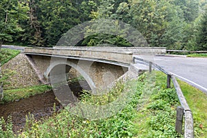 Stone bridge crosses a stream in Eagle mountains Orlicke hory during summer time.