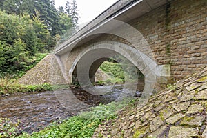 Stone bridge crosses a stream in Eagle mountains Orlicke hory during summer time.