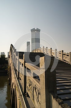 A stone bridge over the canal in Wenzhou, China in Nantang park with a skyscaper in the background