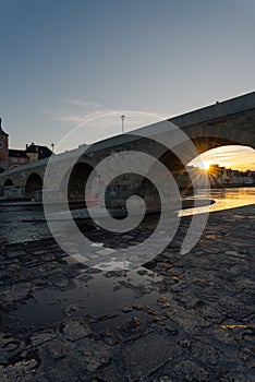 Stone bridge and skyline of Regensburg with setting sun on clear winter day