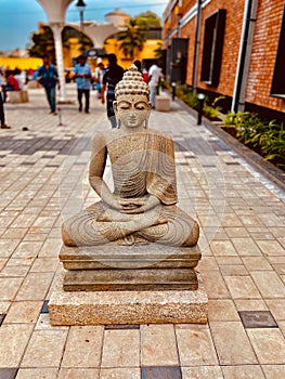 a stone buddha sits on a platform near some people and buildings