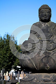 Stone Buddha sitting outdoors on gravestone in Japan