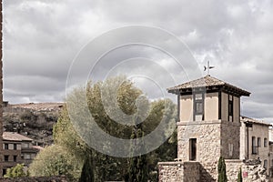 a stone building with a weathervane, surrounded by trees and structures, under a cloudy sky in molina de aragon