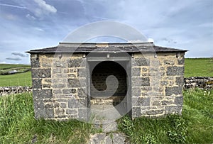 Stone bus shelter, surrounded by plants, dry stone walls, and fields in, Horton in Ribblesdale, UK