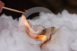 Stone of Calcium carbide calcium acetylide burn with big flame in white snow. Piece of carbide react with water from snow and