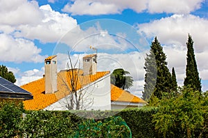 Stone chimneys on rooftops with orange shingles against sky clouds Country house