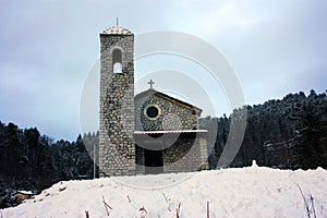 Stone church and bell tower in the mountains in the soft white winter snow