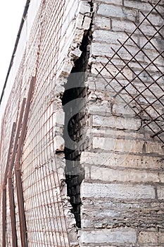 Stone cladding falls off from the brick wall of the building and is held back by metal pipes and mesh.