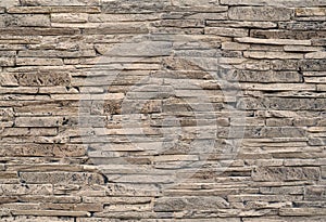 Stone cladding wall made of striped stacked slabs of natural brown rocks stained with black