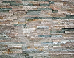 Stone cladding wall made of striped stacked slabs of natural rocks.. Colors are various, from dark green to white.