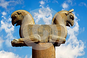 Stone column sculpture of a Griffin in Persepolis against a blue sky with clouds. Ancient Achaemenid Kingdom.