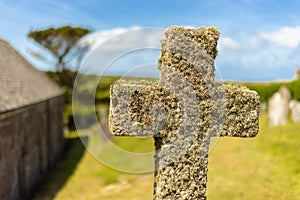A stone cross overgrown with moss in the sunshine in Cornwall.