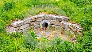 Stone drain and a round metal grid with dry leaves in a park surrounded by green vegetation