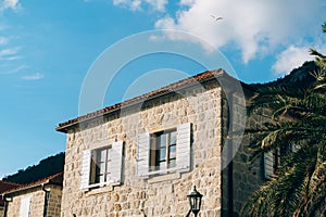 Stone facade of the building with shutters on the windows and a red tiled roof