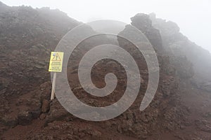 stone fall warning sign on a foggy day on the pedestrian path to the top of the mount vesuvio volcano.  Naples, Italy.