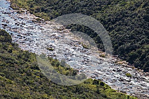 Stone Filled River Flowing Through Steep Tree-Lined Valley