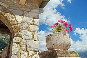 Stone flowerpot with flowers against the blue sky. Ancient Church of Our Lady of the Rocks, Montenegro