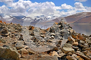 Stone formations in front of the Yamdrok Lake, reflecting the brown colors of Mt. Naiqinkangsang against a blue clear