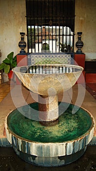 stone fountain, in old mexican house, latin america, with decorated tiles, roof tiles, surrounding vegetation