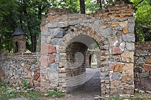 Stone gate in the archway vista and a brick wall with a miniature tower in the style of a medieval castle in park
