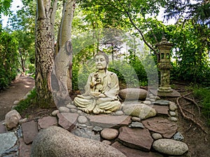 Stone Gautama Buddha decorative statue in a garden under green leaves. Outdoor Garden decor concept. Abakan