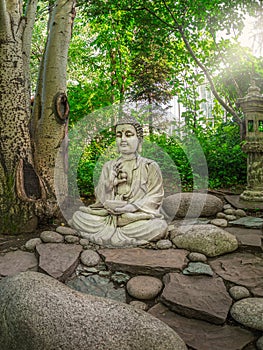 Stone Gautama Buddha decorative statue in a garden under green leaves. Outdoor Garden decor concept. Abakan, vertical view