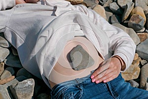 Stone on the girl`s belly. Unrecognizable girl lying on a stone beach in the fall.