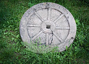 Stone granite wheel with rusted metal rim isolated on green grass.